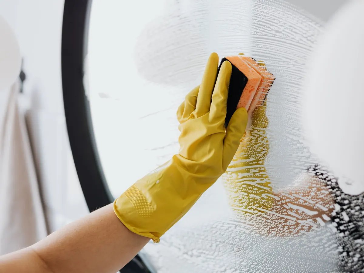 Gloved hand scrubbing a surface with a sponge and foam